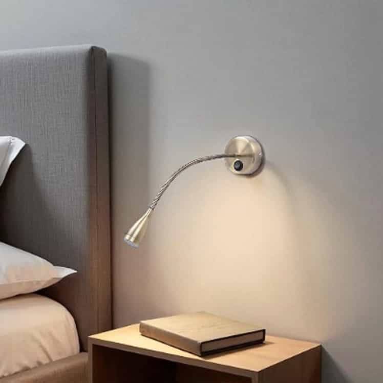 Antique finish flexible bedside reading light mounted on the wall next to a bed and over a bedside table 