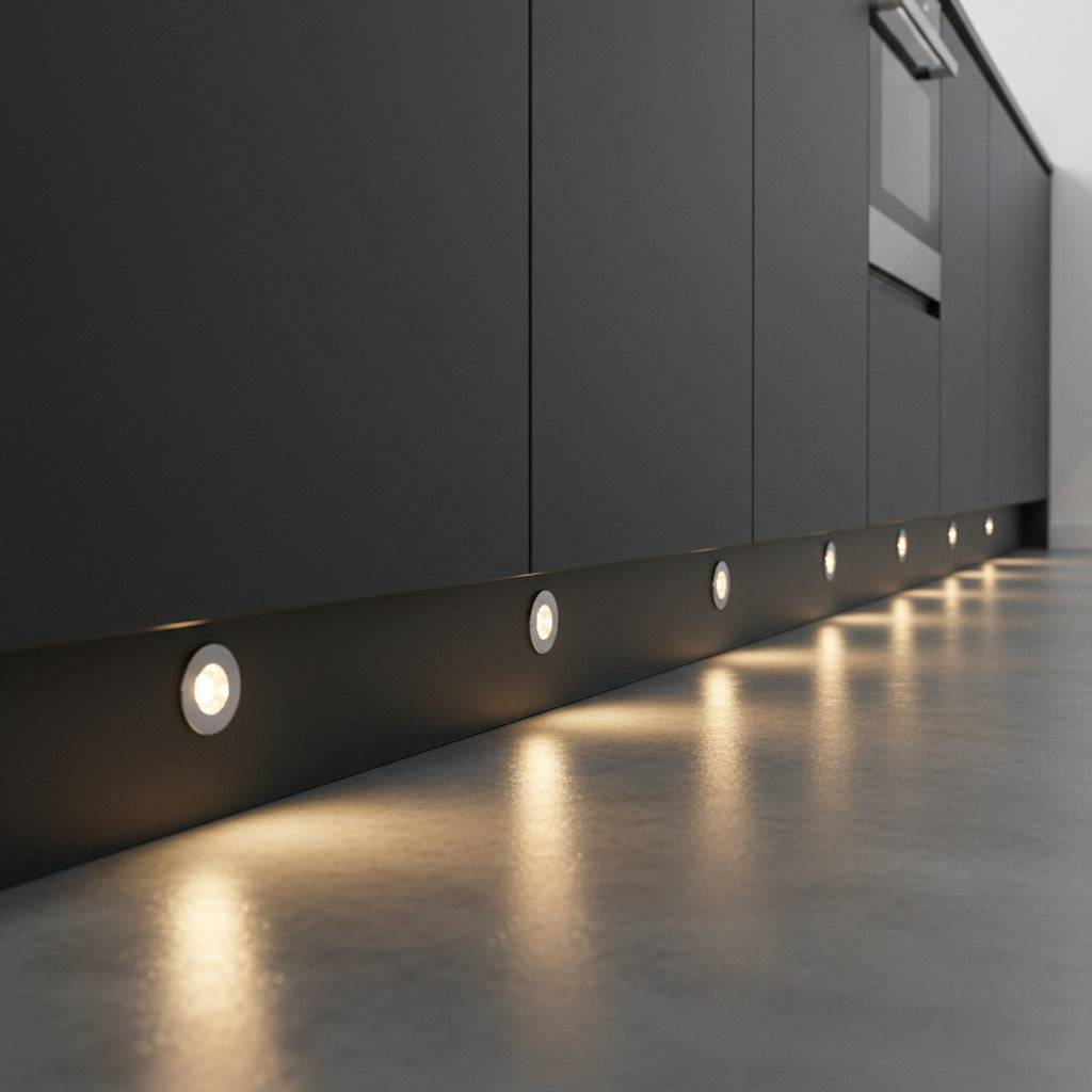 Chrome LED plinth lights mounted at low level in a dark grey kitchen plinth. 