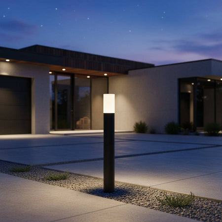 Black driveway bollard light illuminating access to the garage of a modern home