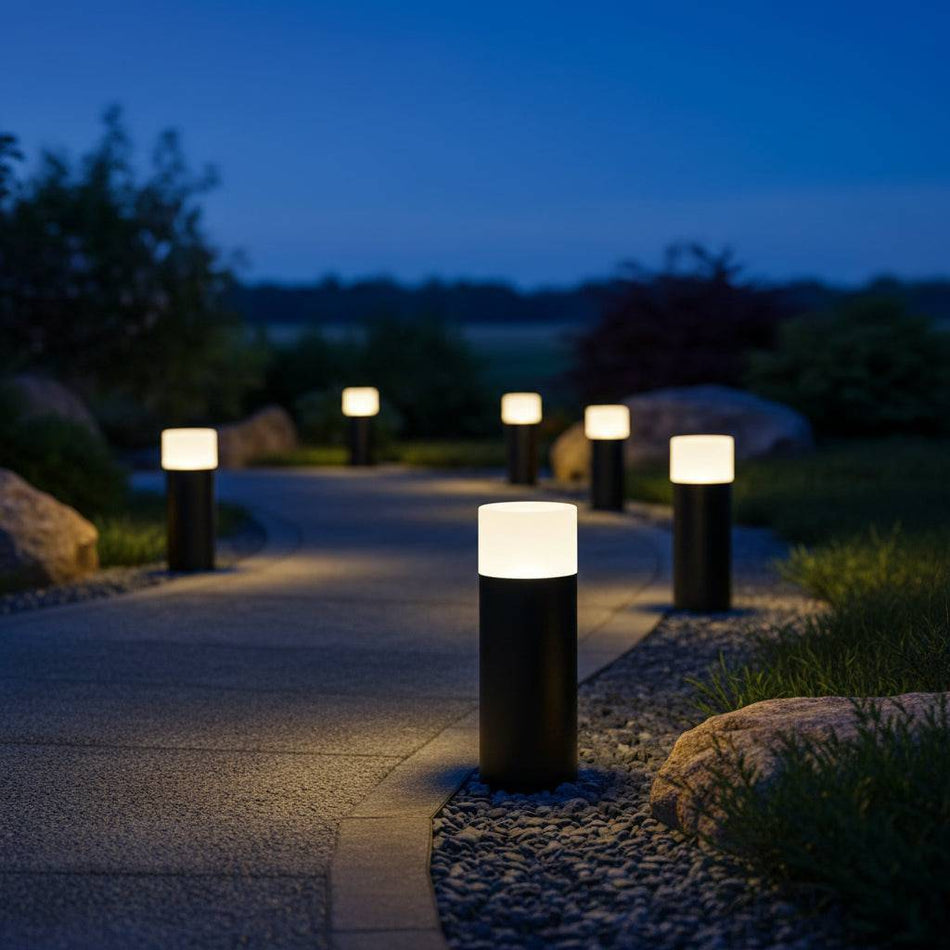 black small bollard light installed in a line along a curved pathway at night. 