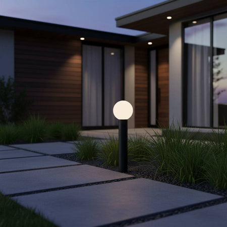 Black illuminated bollard on a grey pathway leading to a modern house