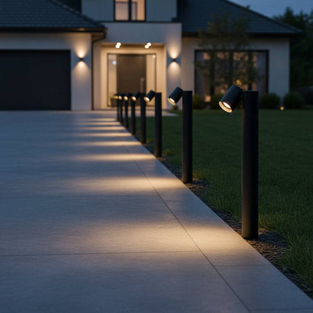 Black adjustable bollard light on driveway leading to a modern well lit house