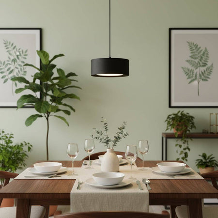 Black circular pendant light above a dining room table with cutlery and crockery laid and plants and pictures in the back ground