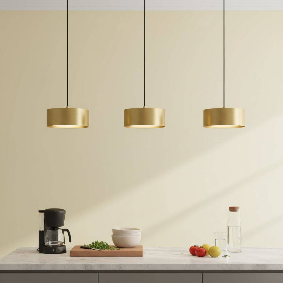 Gold pendant light above a kitchen worktop with fruit and coffee machine against a pale background