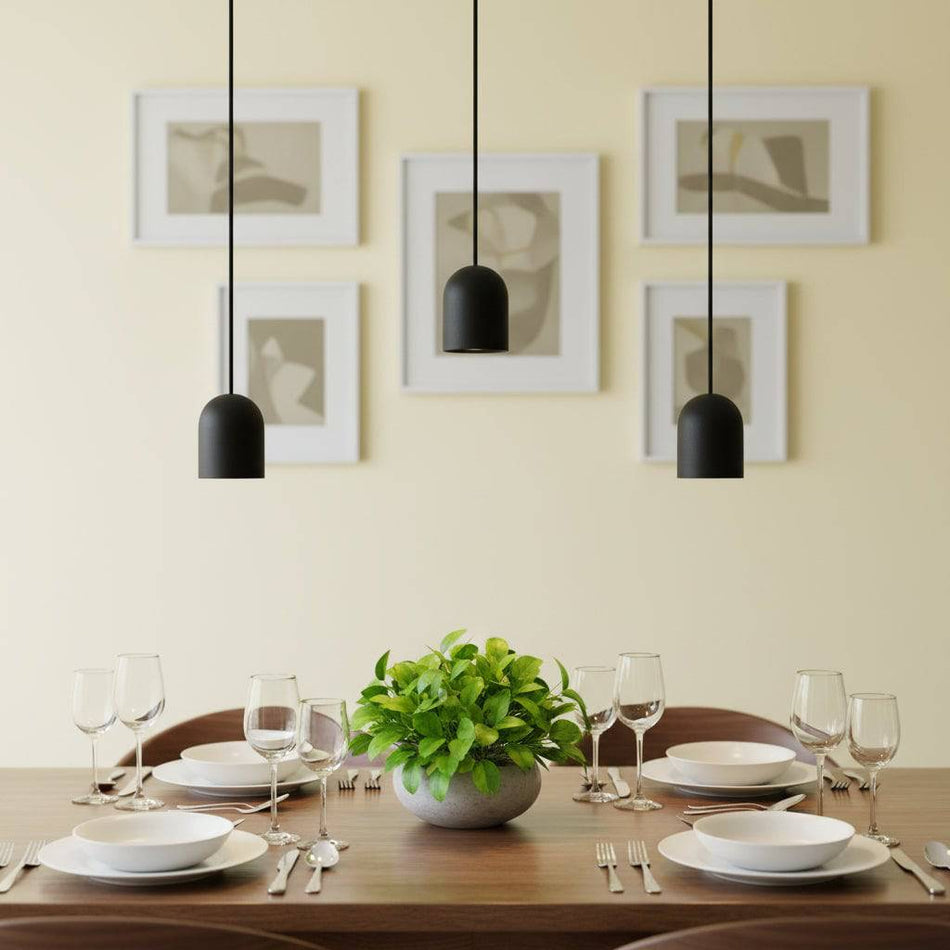 Black small pendant light above a dining room table with cutlery and china and glasses against a pale yellow background