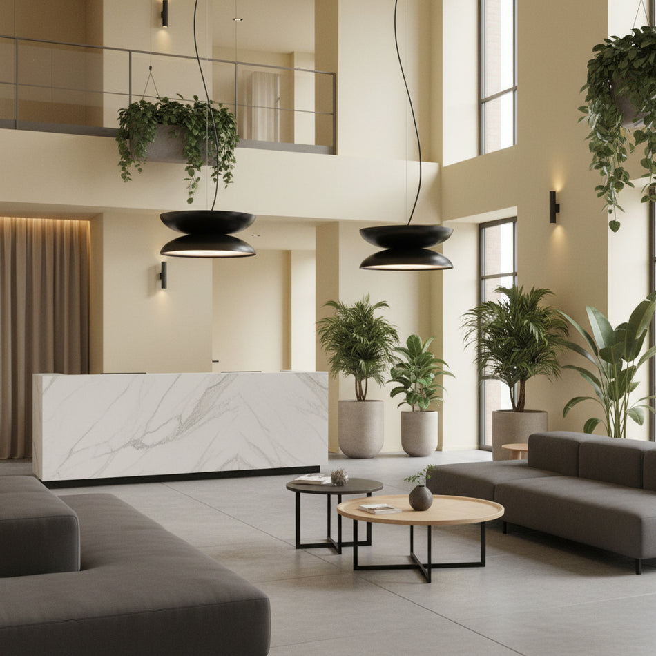 Statement pendant light in an open plan hotel reception with pale yellow walls and plants and furniture.