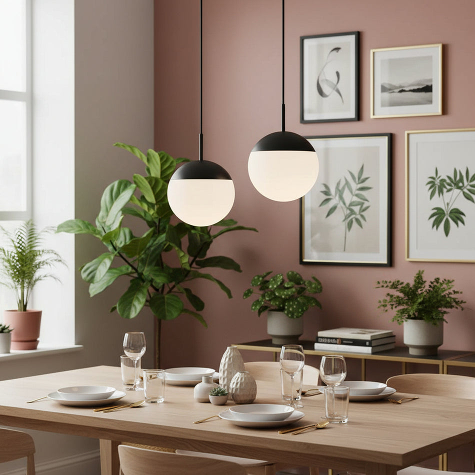 Globe pendant lights above a dining room table with plants and pictures on a pale pink background