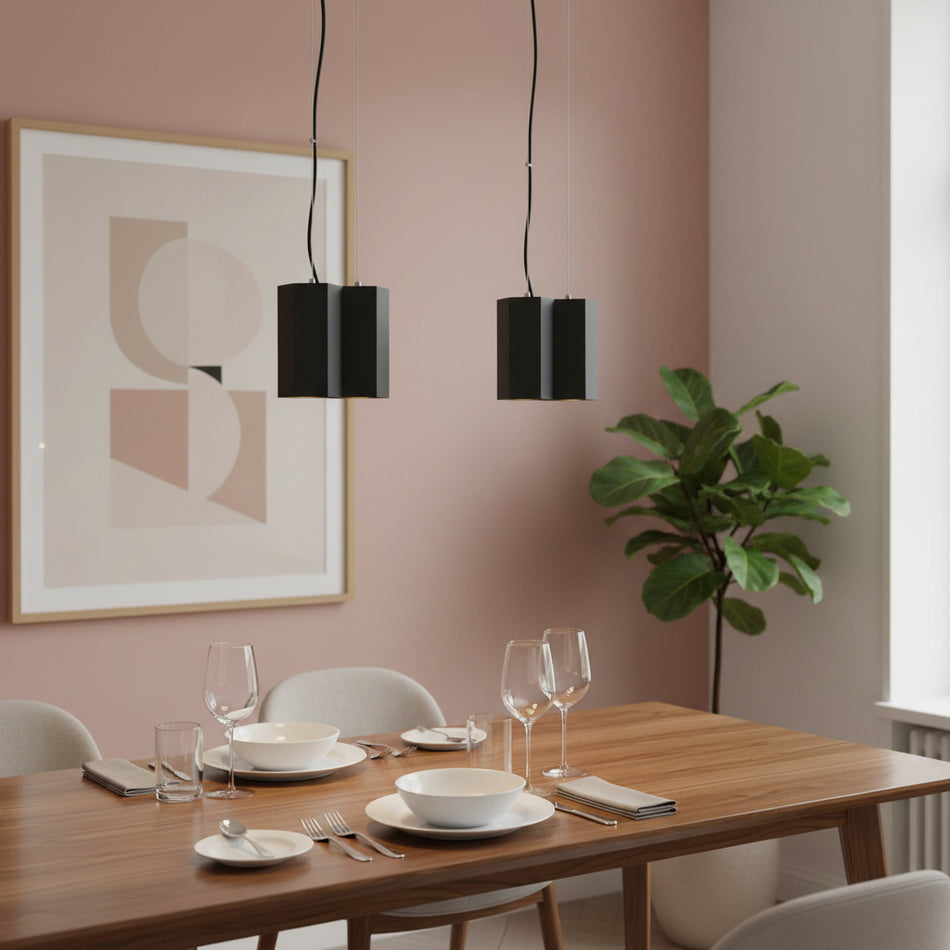 Black pendant lamp above a dining room table with chairs and cutlery glasses and a picture against a pale pink background