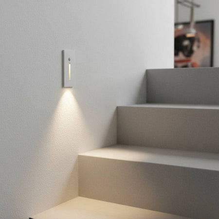 white motion sensor step light installed on a white wall next to some white stairs 