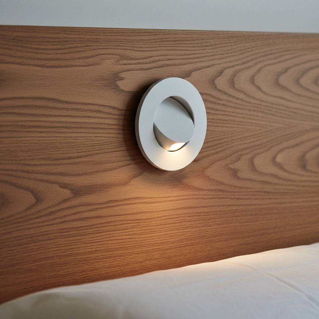 White recessed bedside reading light mounted into a wooden headboard above a bed