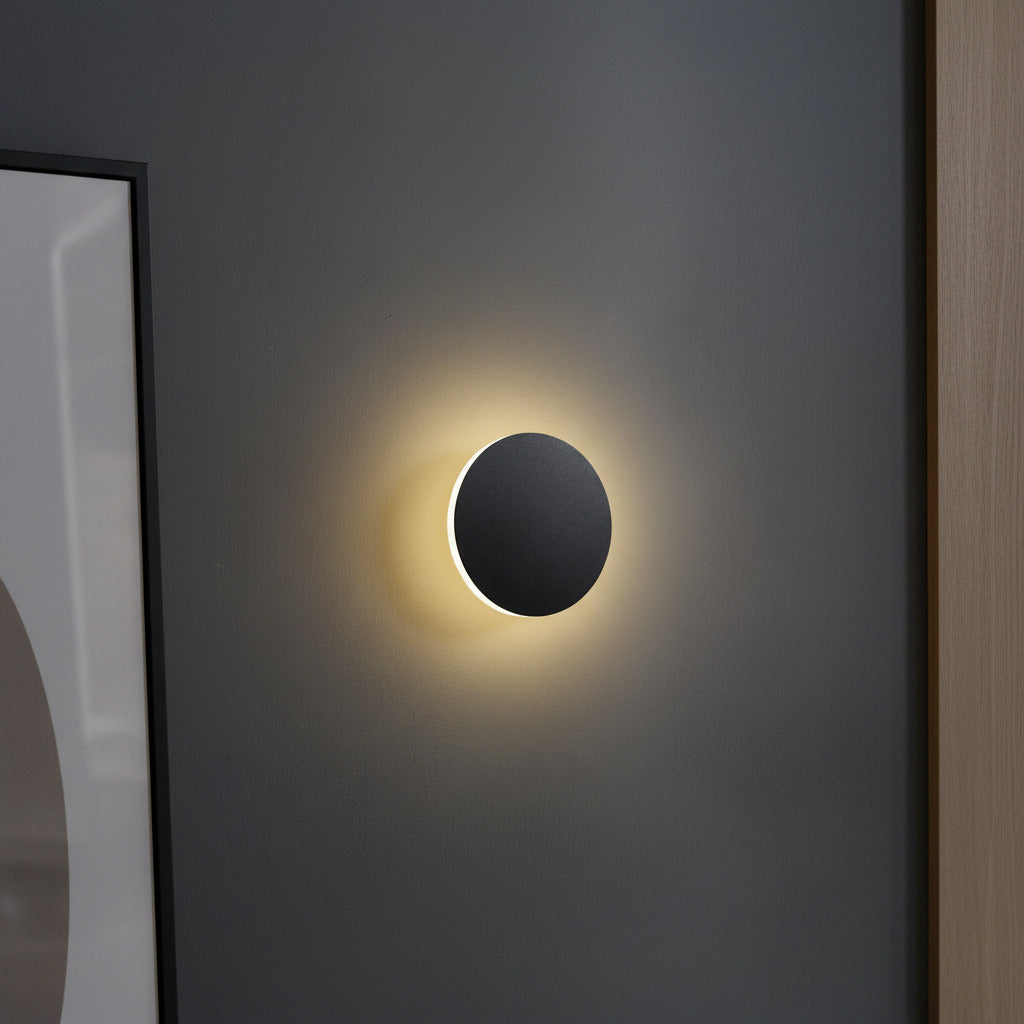 round black modern wall sconce mounted on a grey wall next to a mirror 