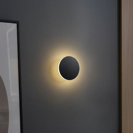round black modern wall sconce mounted on a grey wall next to a mirror 