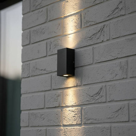 black outdoor up and down wall light mounted on a grey brick wall 