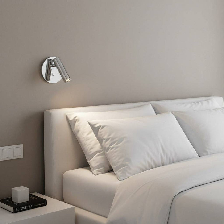 Polished chrome recessed bed reading lamp mounted next to a bed on the wall in a modern bedroom 
