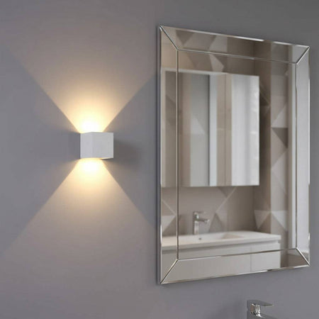 white modern bathroom wall light mounted on the wall next to a bathroom mirror 