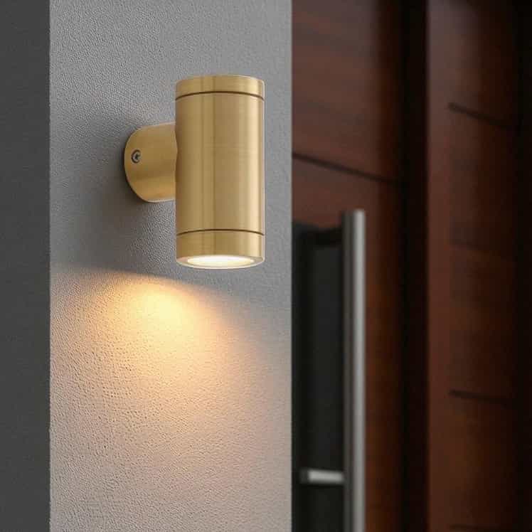 exterior brass wall lamp mounted on a white textured wall next to a wooden front door
