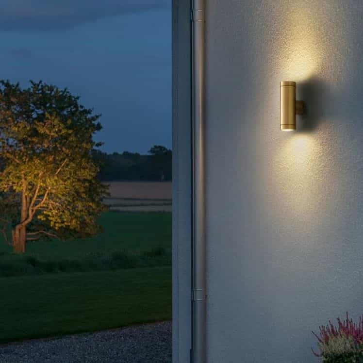 brass up down outdoor wall light mounted on a white textured wall outside a house