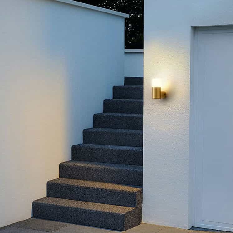 brass outdoor wall light mounted on a white exterior wall next to a stairway