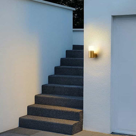 brass outdoor wall light mounted on a white exterior wall next to a stairway