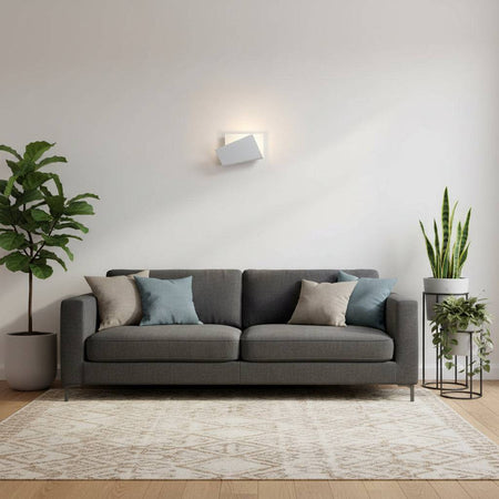 White indoor wall sconce on a white wall above a two seater sofa with plants either side