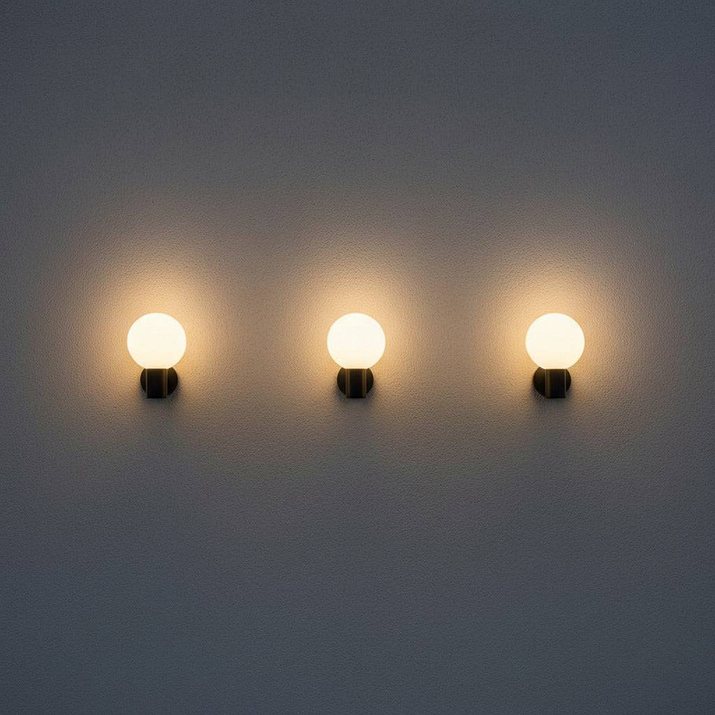 black globe outdoor wall light with 3 lights mounted in a row along a white wall outside