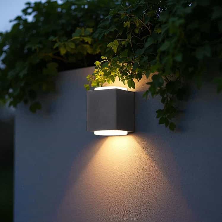 black outdoor up and down light mounted on an outdoor wall with greenery above 