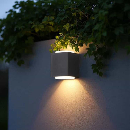 black outdoor up and down light mounted on an outdoor wall with greenery above 