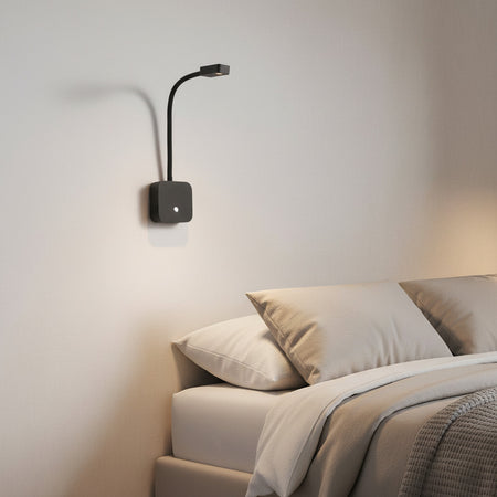flexible black bedroom reading light with USB ports mounted over a bed 