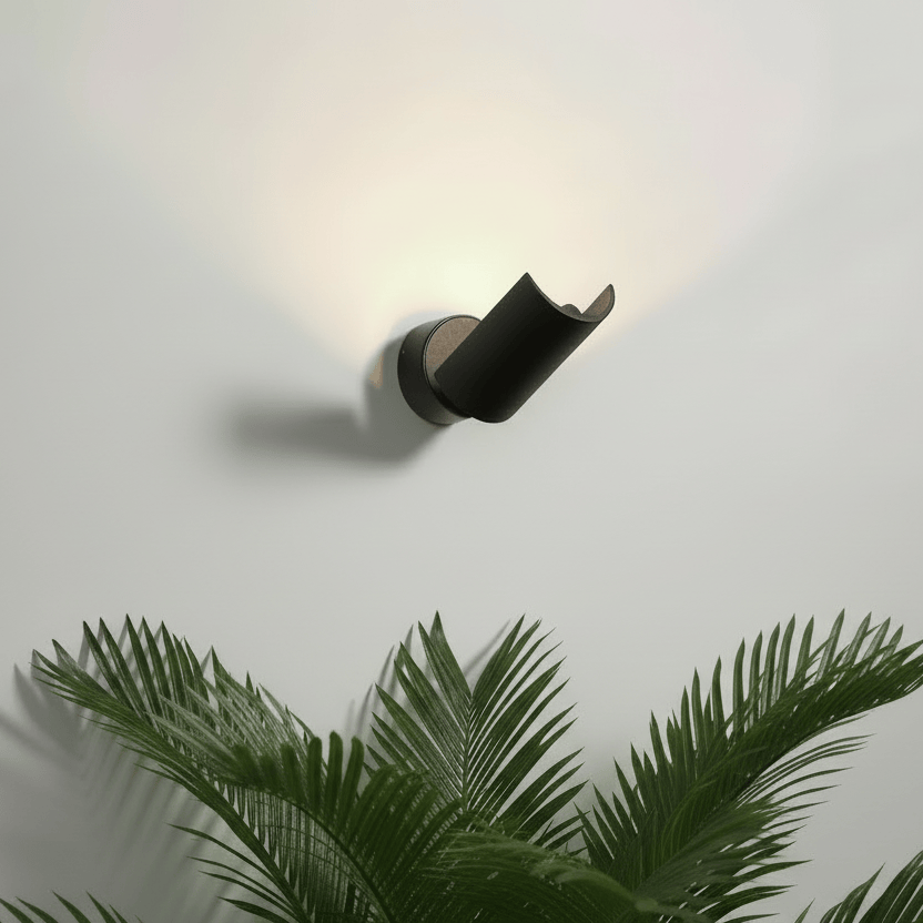 Black indoor wall uplighter on a pale grey wall above a fern plant