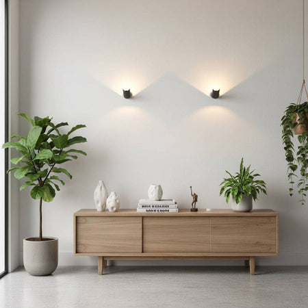 Black indoor wall uplighter on a grey wall with a side board and plants below the light