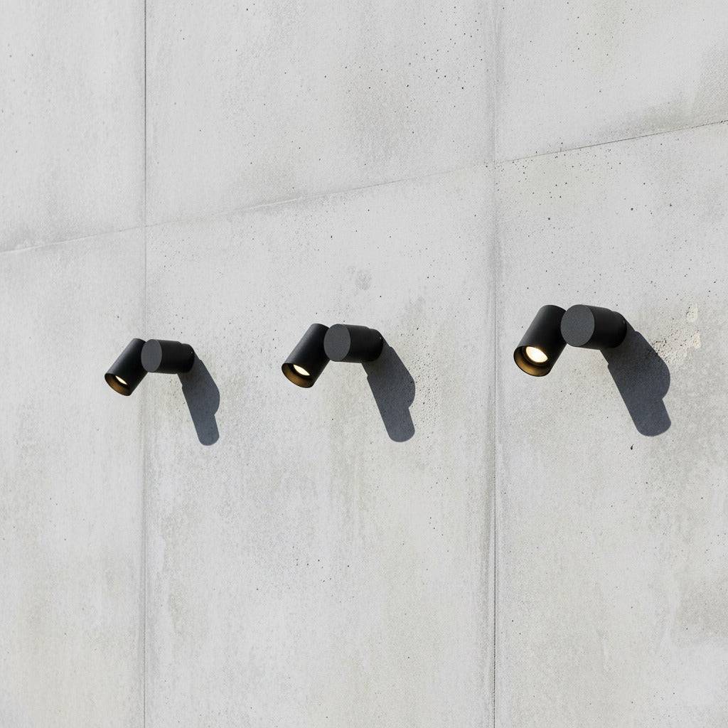 black exterior spotlight wall light showing 3 lights mounted on a concrete wall in a row 