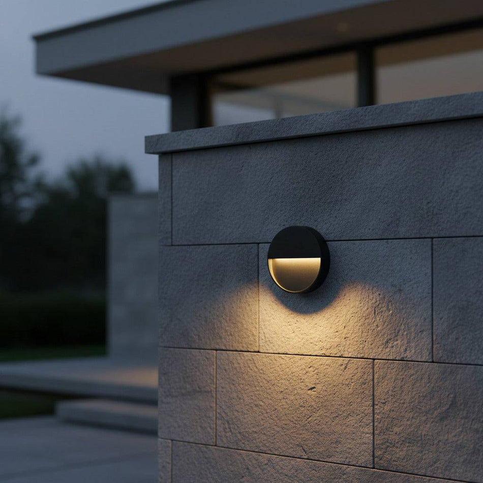 black flush mount wall sconce mounted on a stone wall outside a modern home