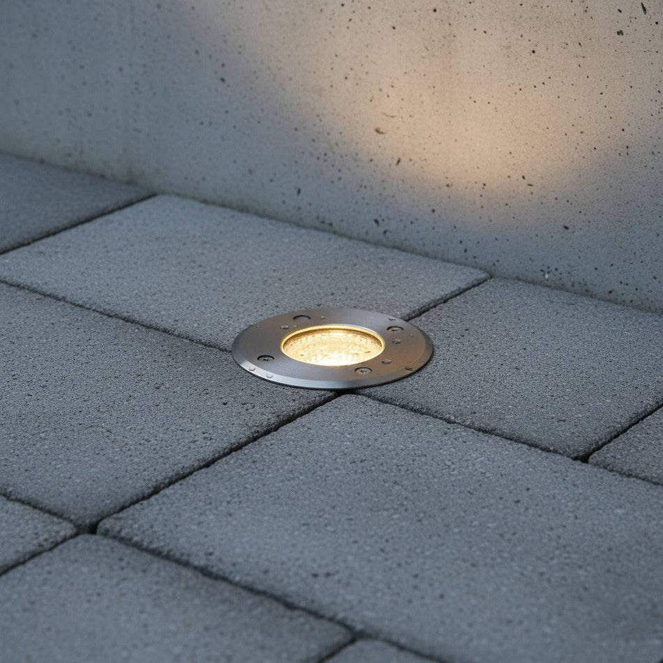 silver exterior ground light mounted in the floor next to an outside wall 