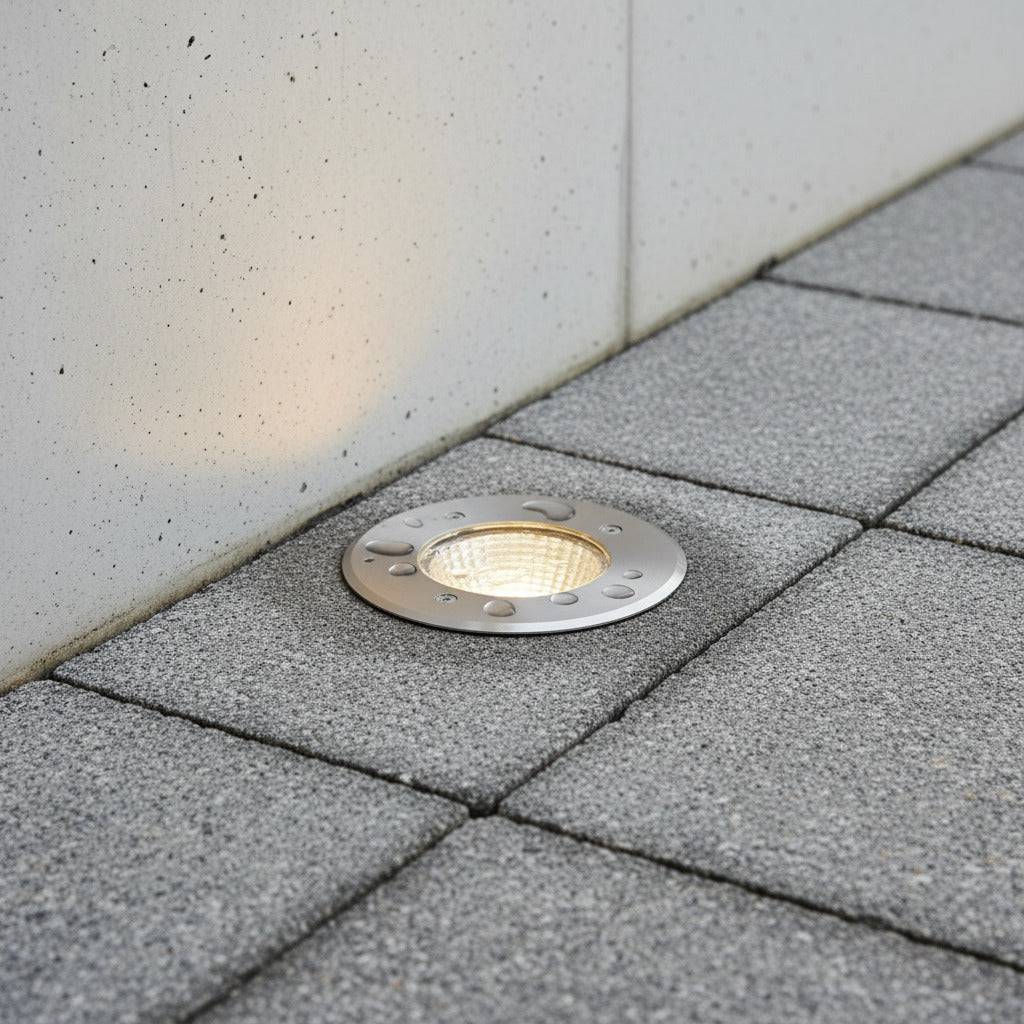stainless steel outdoor ground lamp mounted in the ground next to a wall 