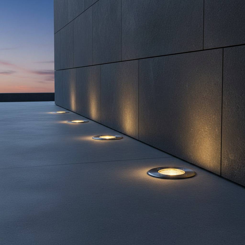 stainless steel outdoor ground lamp mounted in a row next to a wall outside