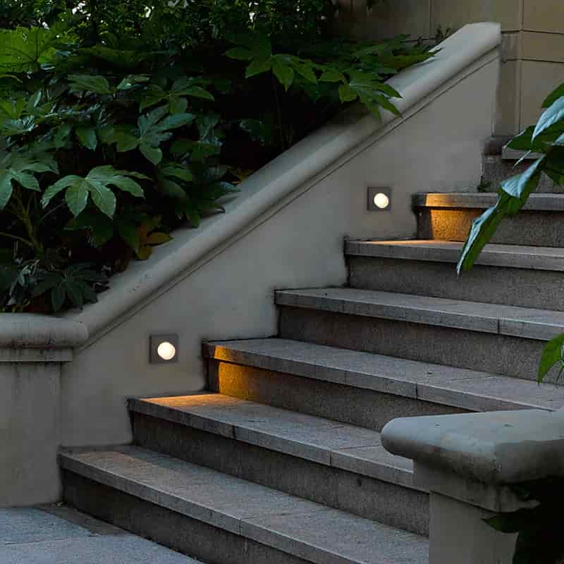 black outdoor step light mounted in the wall alongside some stone steps 