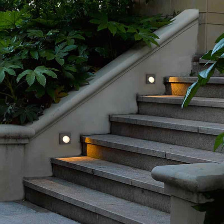 black outdoor step light mounted in the wall alongside some stone steps 