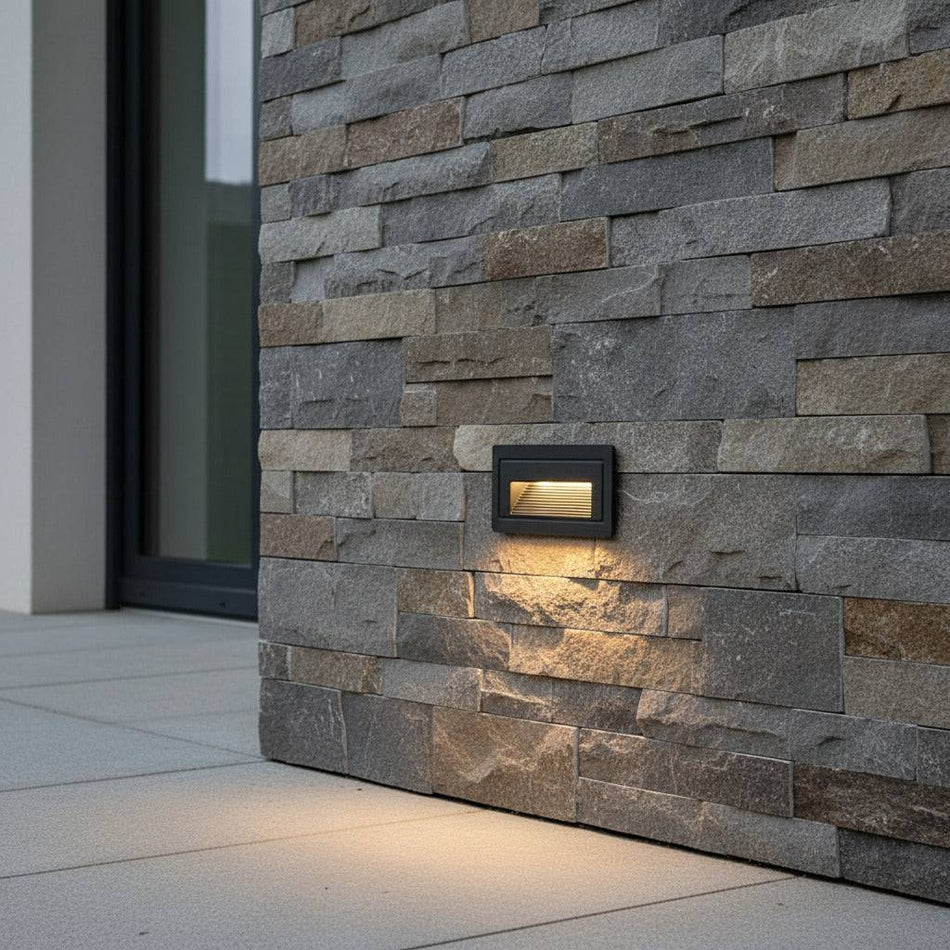 black low level wall light mounted on a stone wall outside of a modern house