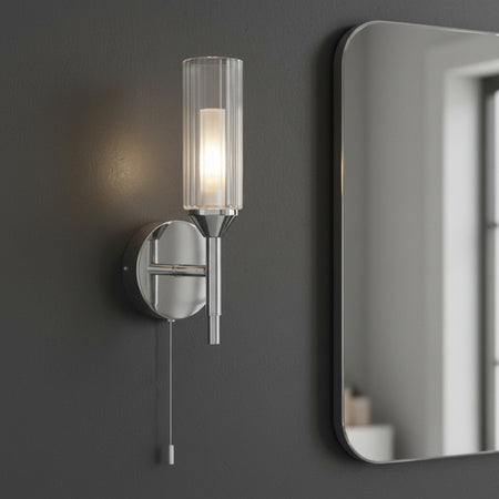 chrome bathroom wall light with pull cord mounted on a grey bathroom wall 