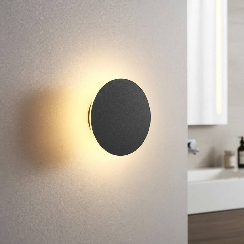 Ultra Beam Lighting Ltd round black bathroom sconce with warm 3000K LED glow mounted on a neutral wall