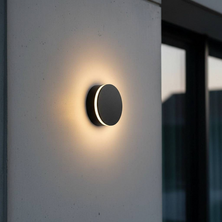 Ultra Beam Lighting Ltd round black LED outdoor wall lamp with a warm halo glow on a modern exterior wall