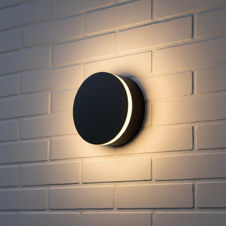 Ultra Beam Lighting Ltd 12W round black LED outdoor wall lamp with a glowing halo effect on a white brick wall.