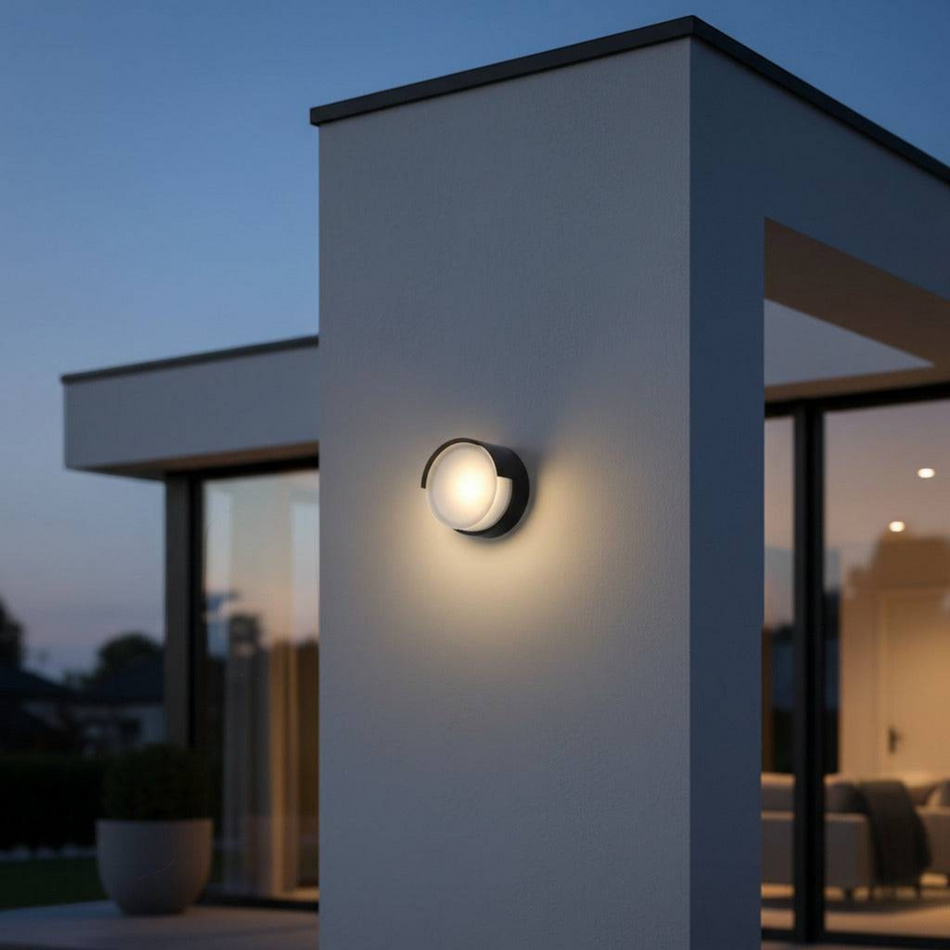 Ultra Beam Lighting Ltd 6W round black LED exterior wall light with warm glow mounted on a modern home facade