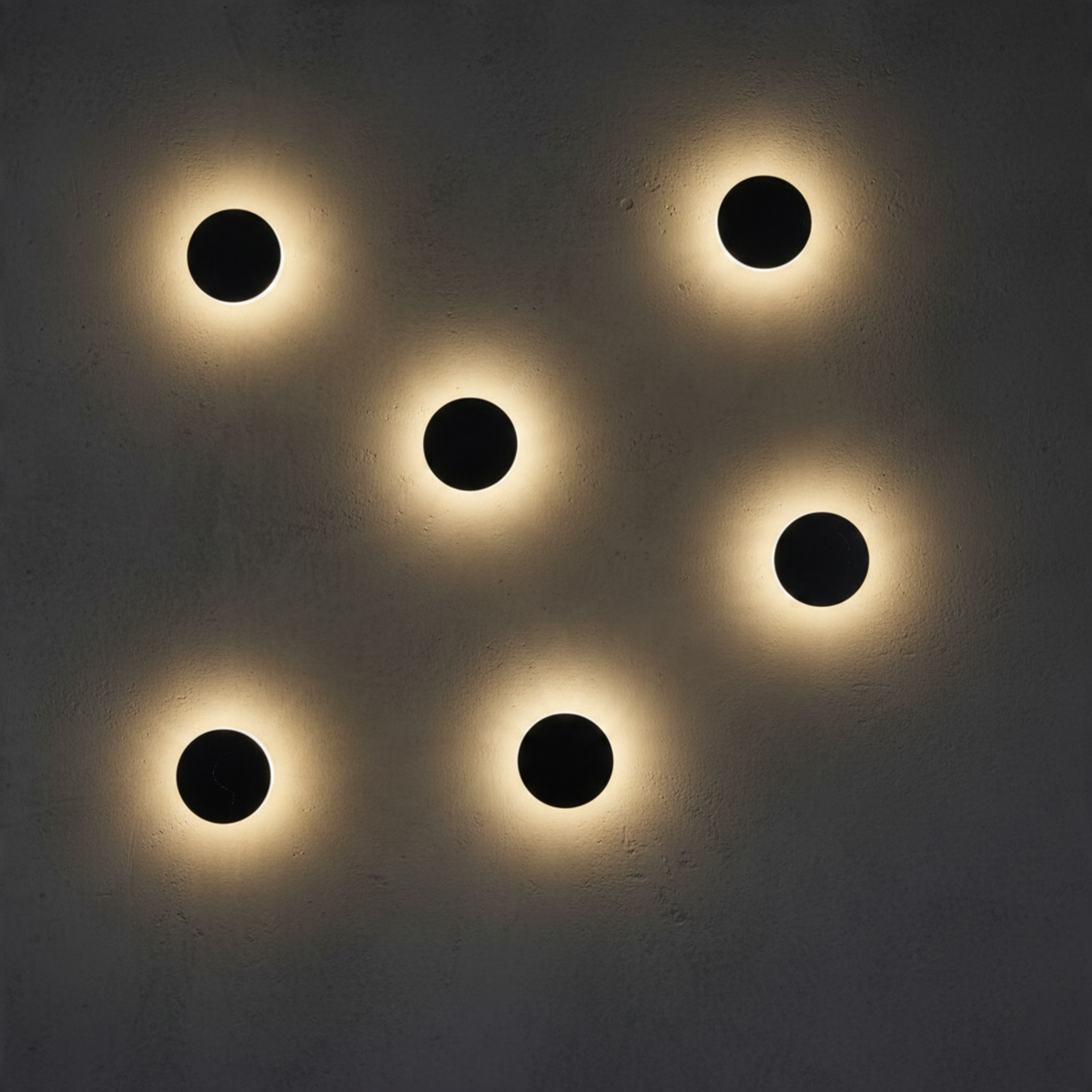 Ultra Beam Lighting Ltd round matte black LED wall sconces creating a warm halo light effect on a textured wall