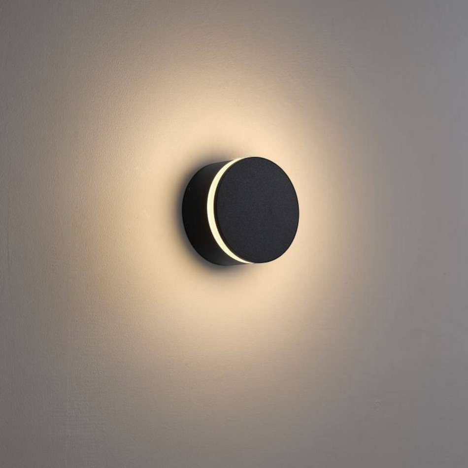Ultra Beam Lighting Ltd round black outdoor LED wall lamp emitting a warm white halo glow on a neutral wall
