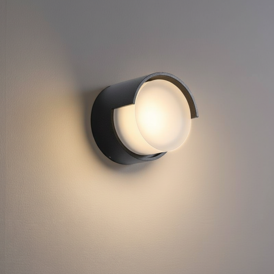 Ultra Beam Lighting Ltd round black outdoor LED wall lamp with a frosted diffuser casting warm white light.