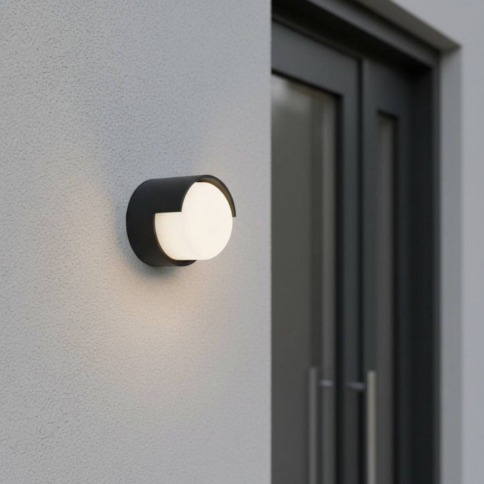Ultra Beam Lighting Ltd round black LED outdoor wall lamp with a frosted diffuser mounted on a grey exterior wall.