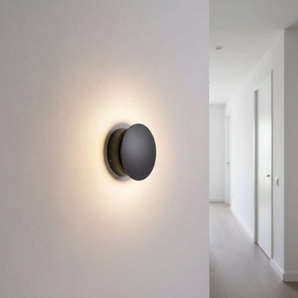 Ultra Beam Lighting Ltd 6W round black decorative indoor wall light fixture emitting a warm glow on a white wall