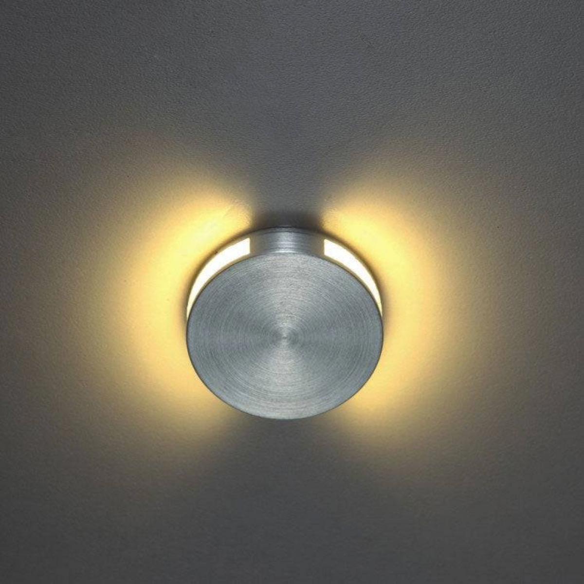 Ultra Beam Lighting Ltd Halo round brushed aluminum LED step light emitting a soft warm glow on a dark wall