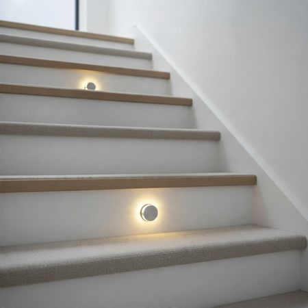 Ultra Beam Lighting Ltd round recessed LED step light in brushed aluminum installed on a carpeted staircase.